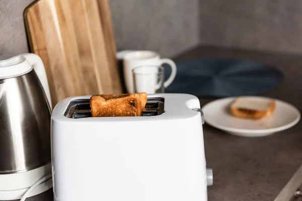 selective focus of toaster with toasts, electrical kettle and cutting board in kitchen