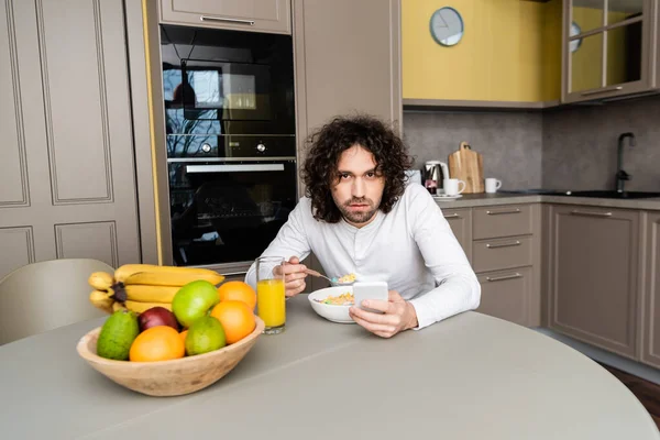 Hombre Serio Mirando Cámara Mientras Desayuna Chatea Teléfono Inteligente Cocina — Foto de Stock