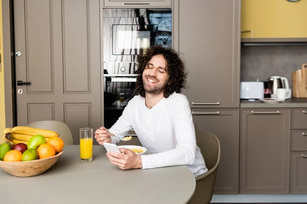 cheerful man chatting on smartphone during breakfast in kitchen