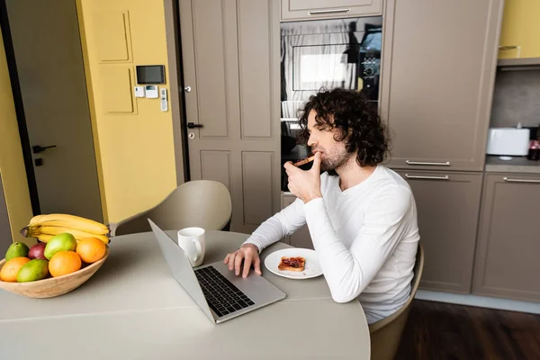 Omtänksam Frilansande Äta Rostat Bröd Medan Tittar Laptop Nära Kaffekopp — Stockfoto