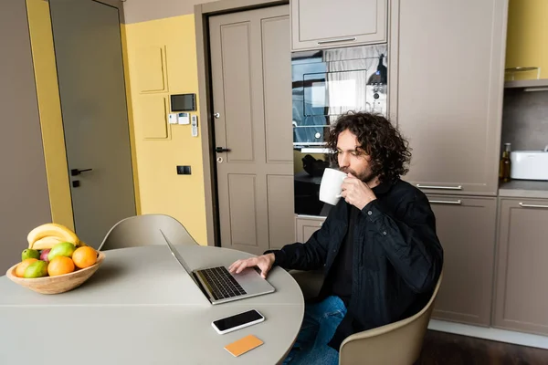 Genç Serbest Çalışan Kahve Içerken Akıllı Telefonun Yanında Bilgisayarla Boş — Stok fotoğraf