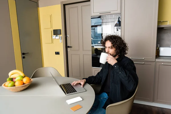 Handsome Freelancer Drinking Coffee While Using Laptop Smartphone White Screen — Stock Photo, Image