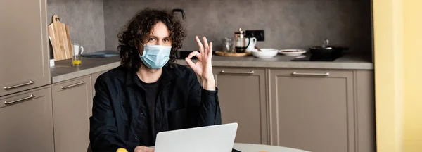 Tiro Panorâmico Homem Máscara Médica Mostrando Gesto Perto Laptop Cozinha — Fotografia de Stock