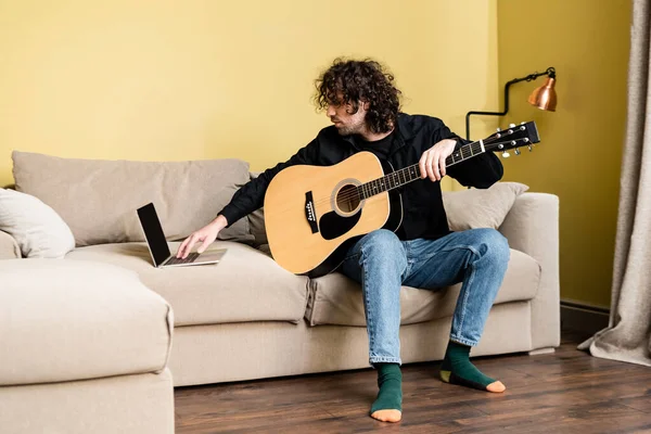 在客厅进行在线教育时 卷曲男子手持音响吉他 使用笔记本电脑 — 图库照片