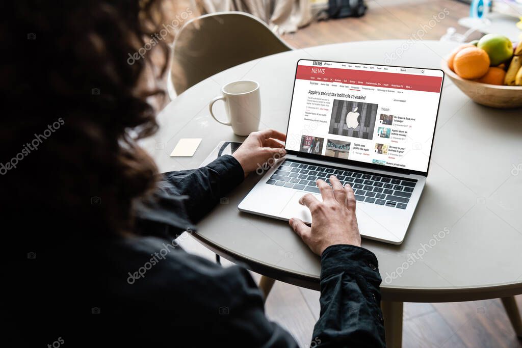 KYIV, UKRAINE - APRIL 25, 2020: back view of freelancer using laptop with BBC news and Apple logo on screen near coffee cup, sticky notes and fruits