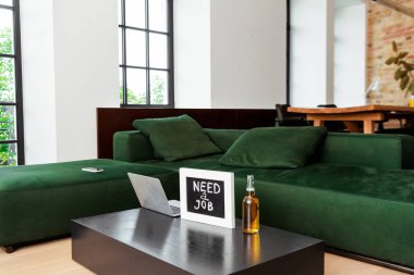 laptop near chalkboard with need a job lettering and bottle of beer near modern sofa clipart