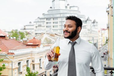 Neşeli Afrikalı Amerikalı adam balkonda bira şişesi tutuyor. 