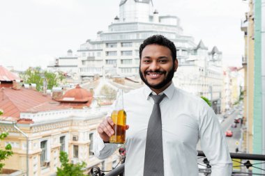 Gülümseyen Afrikalı Amerikalı adam balkonda bira şişesi tutuyor. 