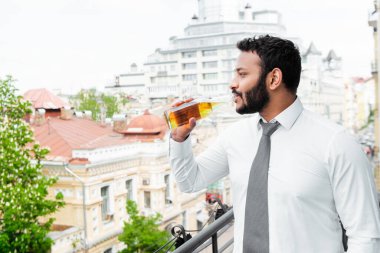 Balkonda bira içen takım elbiseli Afrikalı Amerikalı adamın yan görüntüsü. 