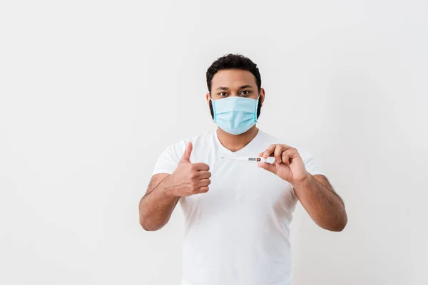 医療用マスクを着たアフリカ系アメリカ人男性がデジタル温度計を持って白い壁の近くに親指を立てて — ストック写真