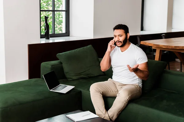 Hombre Afroamericano Emocional Hablando Teléfono Inteligente Gesto Cerca Computadora Portátil —  Fotos de Stock