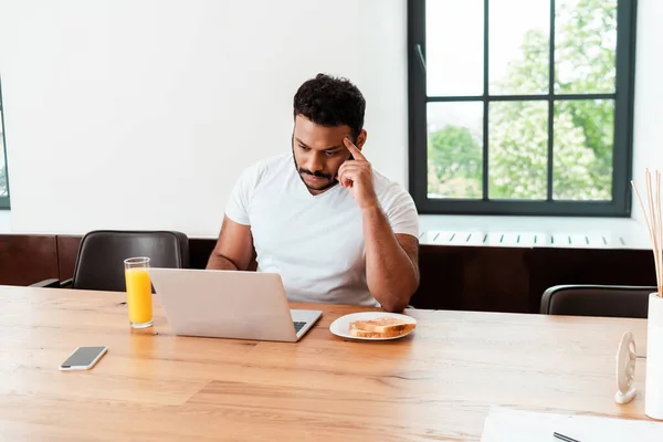 Hombre Afroamericano Pensativo Mirando Portátil Cerca Del Desayuno Teléfono Inteligente —  Fotos de Stock