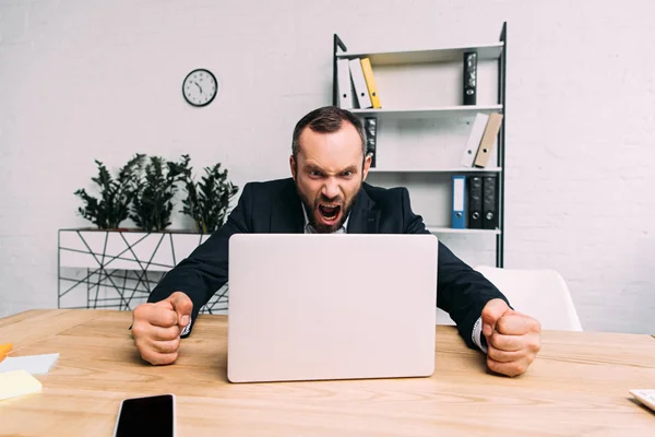 Portrait d'un homme d'affaires surmené en costume hurlant sur le lieu de travail avec un ordinateur portable au bureau — Photo de stock