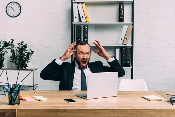 Portrait d'un homme d'affaires surmené en costume hurlant sur le lieu de travail avec un ordinateur portable au bureau — Photo de stock