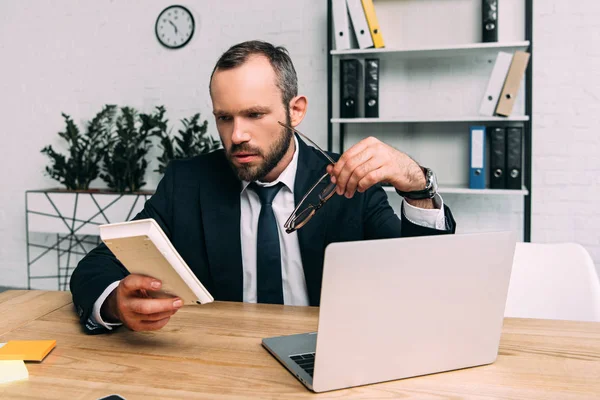 Homme d'affaires concentré avec calculatrice et lunettes sur le lieu de travail avec ordinateur portable au bureau — Photo de stock