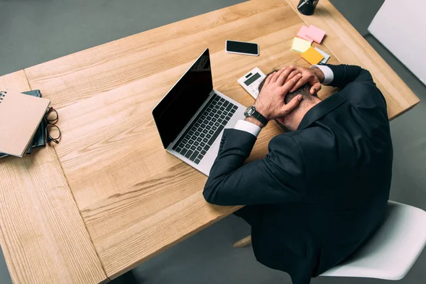 Hochwinkelaufnahme eines gestressten Geschäftsmannes mit Händen auf dem Kopf am Arbeitsplatz liegend mit Laptop im Büro — Stockfoto