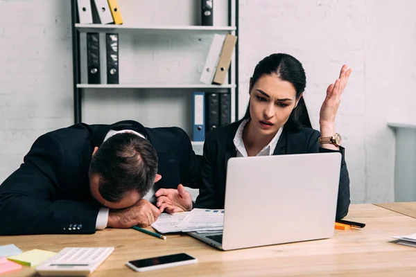 Überlasteter Geschäftsmann und Geschäftspartner am Arbeitsplatz mit Dokumenten und Laptop im Büro — Stockfoto