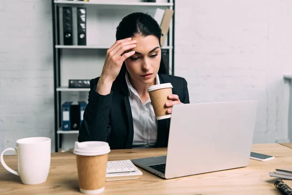 Femme d'affaires fatiguée en costume avec café pour aller travailler sur ordinateur portable sur le lieu de travail au bureau — Photo de stock