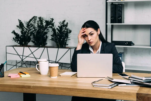 Retrato de empresária sobrecarregada em terno no local de trabalho com laptop e café para ir no escritório — Fotografia de Stock