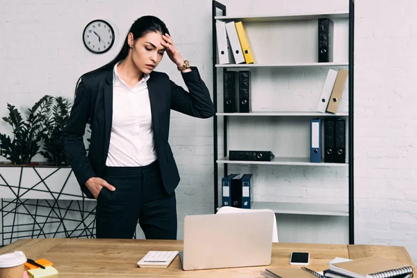 Retrato de mujer de negocios sobrecargada de trabajo de pie en el lugar de trabajo con portátil en la oficina - foto de stock