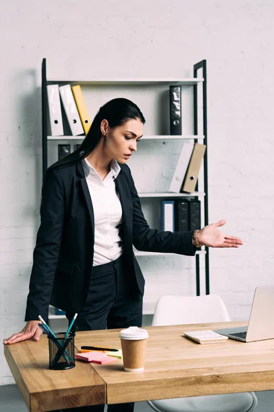 Retrato de mujer de negocios sobrecargada de trabajo de pie en el lugar de trabajo con portátil en la oficina - foto de stock