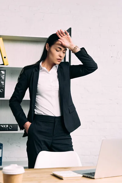 Retrato de mujer de negocios sobrecargada de trabajo de pie en el lugar de trabajo con portátil en la oficina - foto de stock