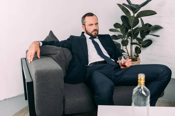 Portrait of businessman in suit with glass of alcohol resting on sofa at coffee table in office — Stock Photo