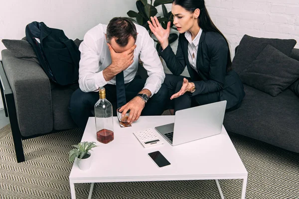 Частковий погляд на напружених бізнес-колег за журнальним столиком з ноутбуком та алкоголем в офісі — стокове фото