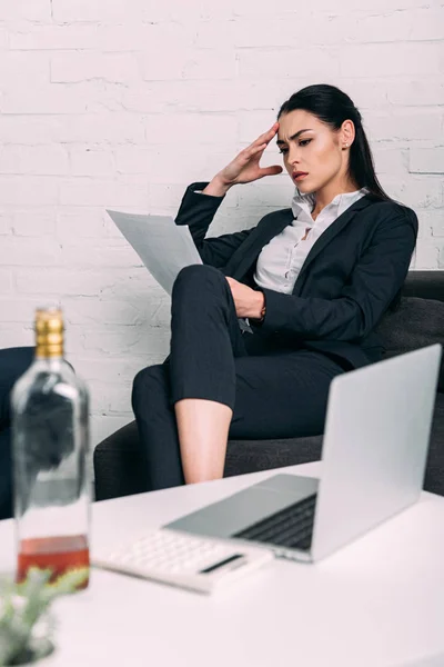 Mujer de negocios enfocada con documentos en la mesa de café con computadora portátil en la oficina - foto de stock