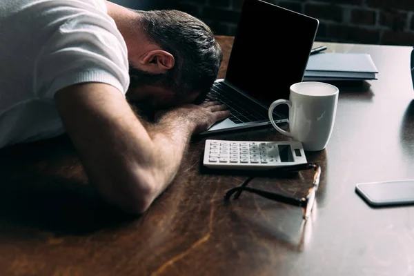 Cansado freelancer remoto acostado en la mesa con el ordenador portátil en la cocina en casa - foto de stock