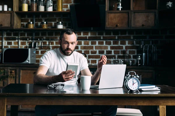 Sorprendido joven mirando la calculadora después de contar las facturas a pagar - foto de stock