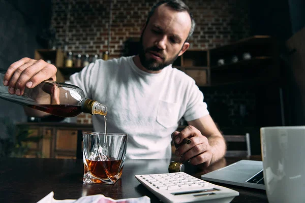 Depressiver junger Mann schüttet Whiskey in Glas auf Küche — Stockfoto