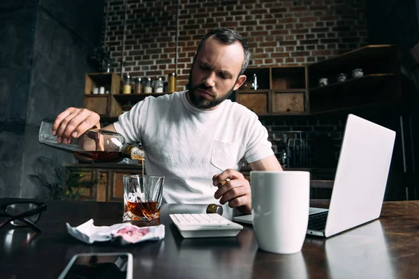 Depressed young man pouring whiskey in glass after breakup with girlfriend — Stock Photo