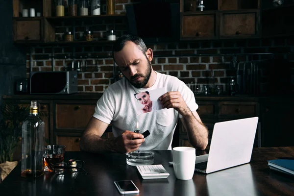 Drunk depressed young man burning photo of ex-girlfriend on kitchen — Stock Photo