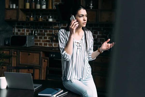 Mujer joven enojada hablando por teléfono en la cocina - foto de stock