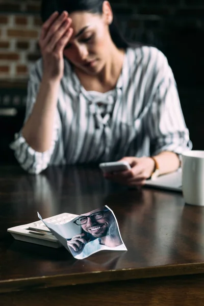 Joven mujer deprimida usando teléfono inteligente con la foto arrugada de ex novio en primer plano - foto de stock