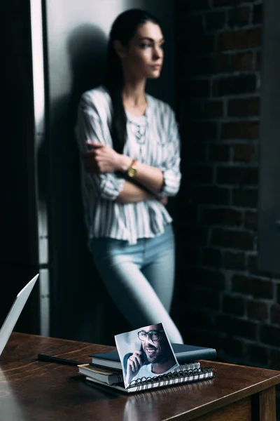 Mujer joven deprimida de pie solo y mirando hacia otro lado con la foto del ex novio en primer plano - foto de stock