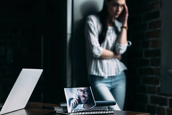 Depressed young woman standing alone and touching head with photo of ex-boyfriend on foreground — Stock Photo