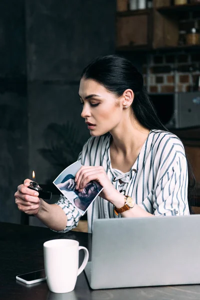 Depressed young woman burning photo card of ex-boyfriend — Stock Photo