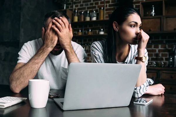 Jovem casal deprimido sentado na cozinha com laptop — Fotografia de Stock