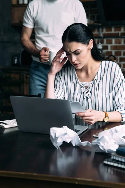 Depressed young woman counting bills while her husband standing behind — Stock Photo