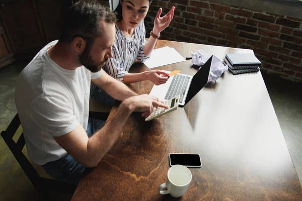 Vista de ángulo alto de la pareja joven contando impuestos y facturas con computadora portátil y calculadora - foto de stock