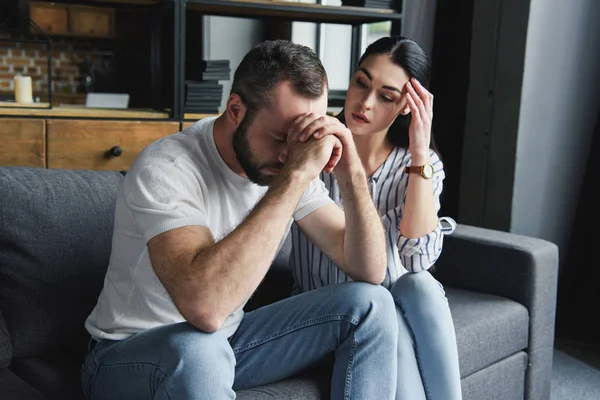 Depresso giovane coppia seduta sul divano a casa dopo litigio e guardando lontano — Foto stock