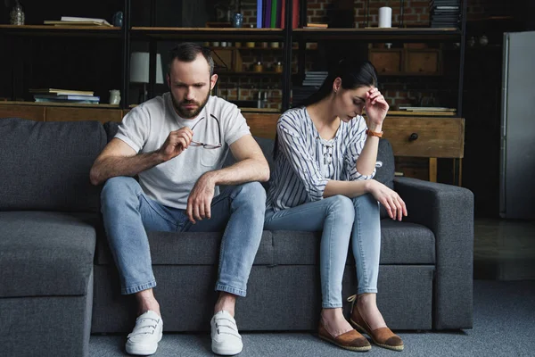 Triste casal sentado no sofá em casa após a briga e olhando para longe — Fotografia de Stock