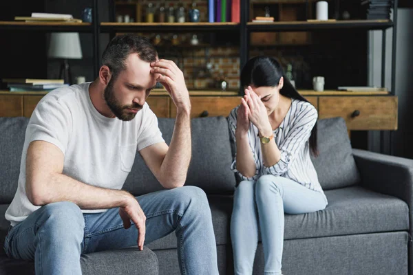 Jovem casal deprimido sentado no sofá em casa após a briga — Fotografia de Stock