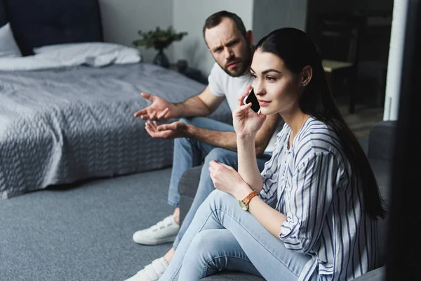 Loco hablando con su esposa mientras ella habla por teléfono en el sofá - foto de stock