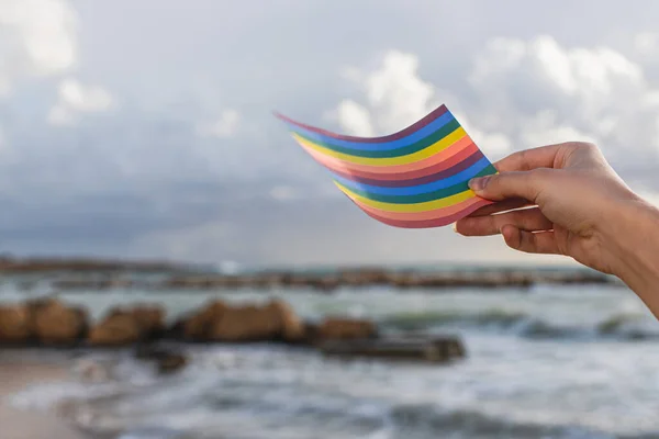 Vista cortada da mulher segurando arco-íris lgbt bandeira perto do mar — Fotografia de Stock