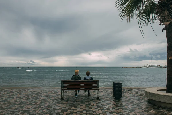 Rückansicht von zwei Personen, die auf einer Bank am Meer sitzen — Stockfoto