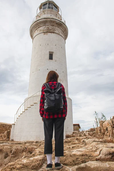 Vista trasera del viajero con la mochila de pie cerca del faro blanco - foto de stock