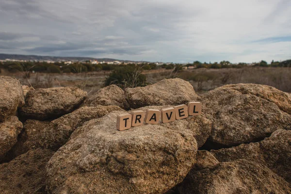 Cubos de madera con letras de viaje sobre rocas contra el cielo - foto de stock